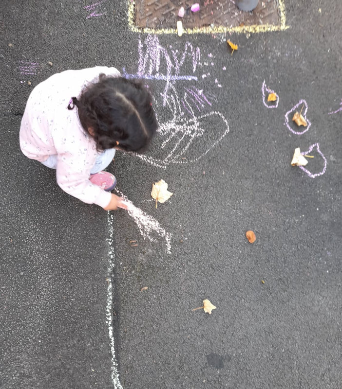 Small child drawing with chalk on the tarmac in the Platt Hall garden