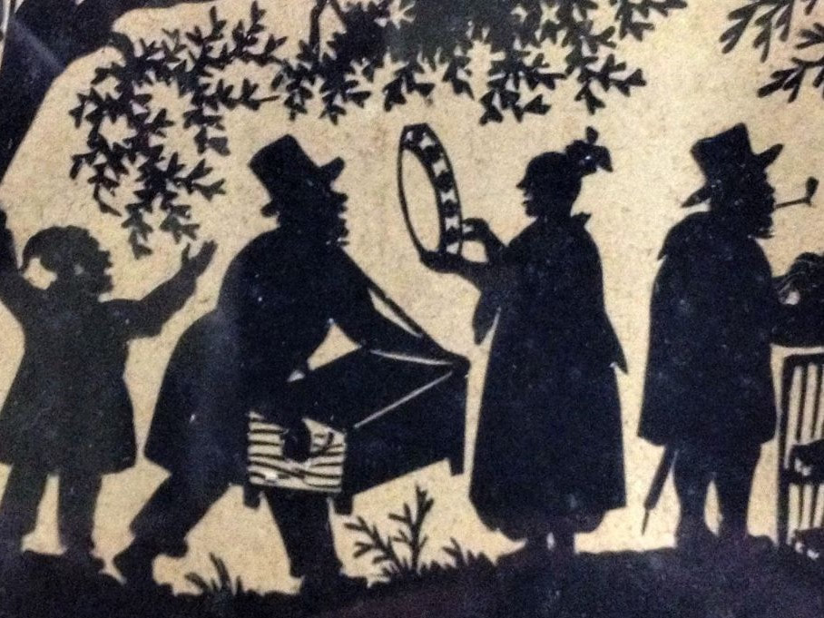 Detail of cut paper picture showing figures in black silhouette with musical instruments.