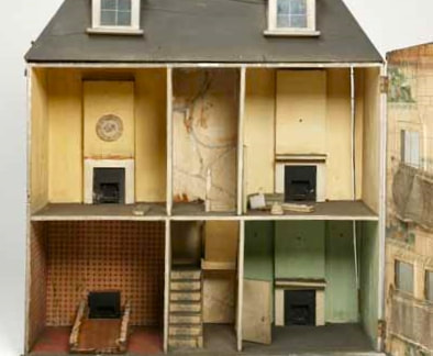 View of the interior of an empty dolls house with stairs and fireplaces.
