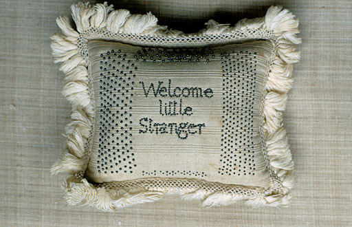 1947.1112 Pincushion and layette, cotton with inscription in pins, 'Welcome little Stranger, MA, CT, 1798'