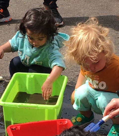Two small children playing with water and soil in the Platt Hall garden