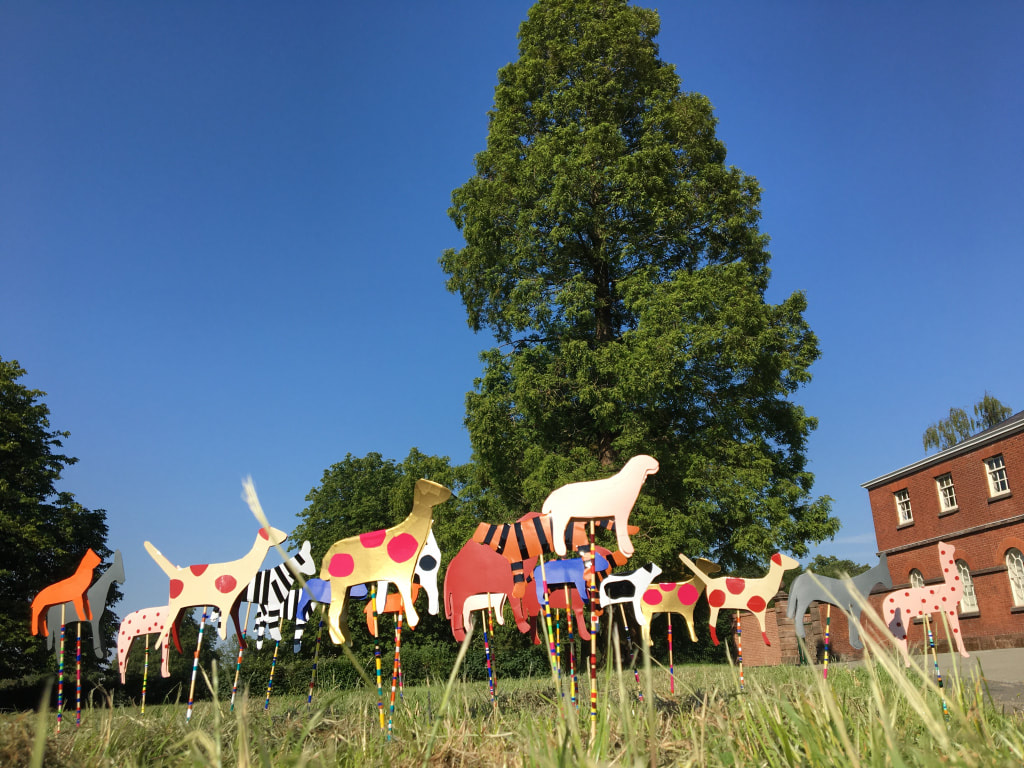View of cardboard cut out Noah's ark animals set in the grass of the park outside Platt Hall.