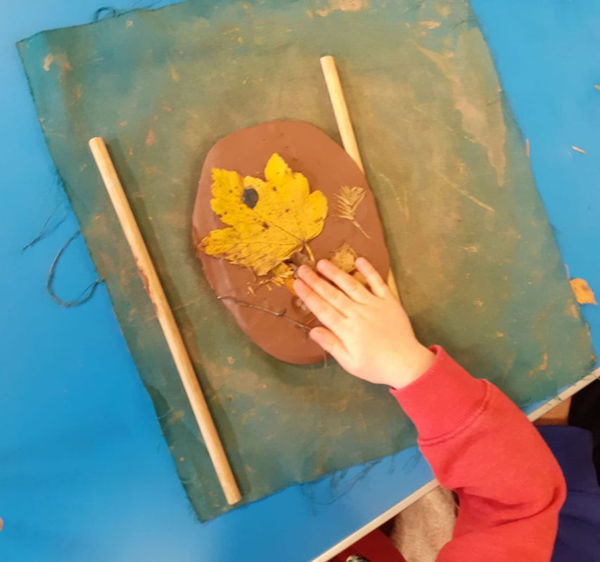 Child's hand pressing a leaf into wet clay.