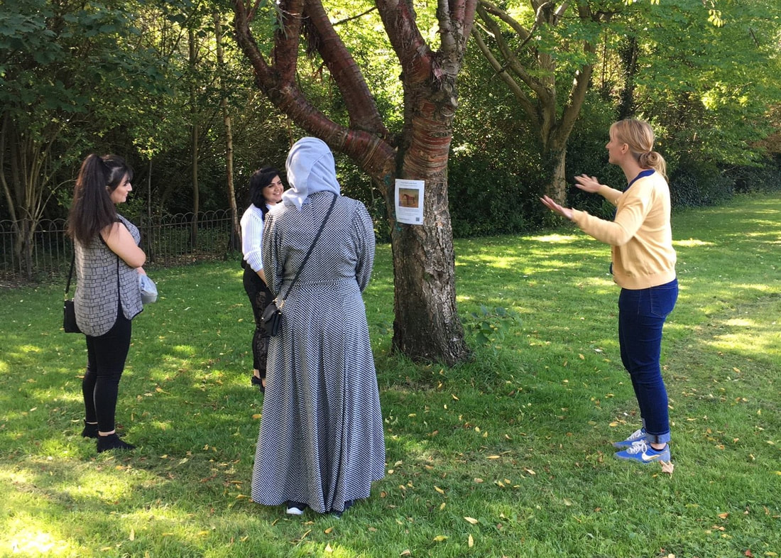 Group of women standing together in the park discussing an image tied to a tree.